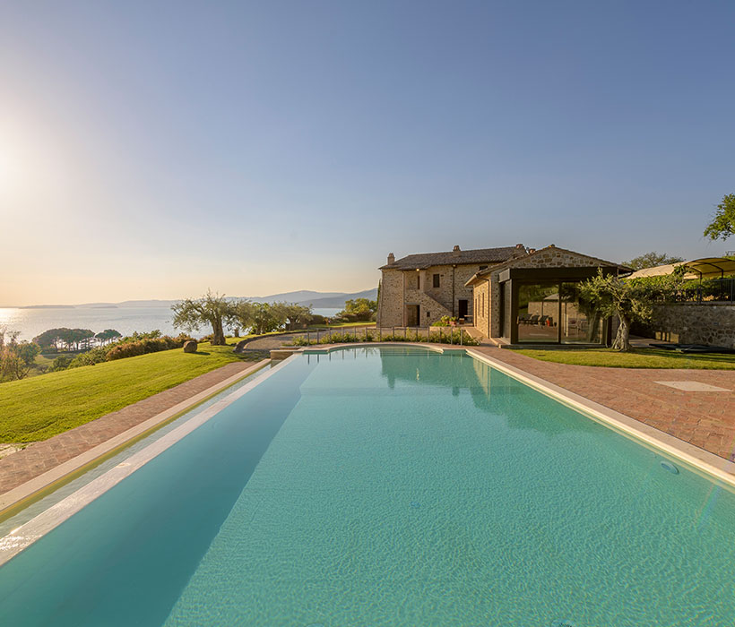 Villa di lusso con piscina a sfioro che si affaccia sul lago e sulle colline al tramonto.