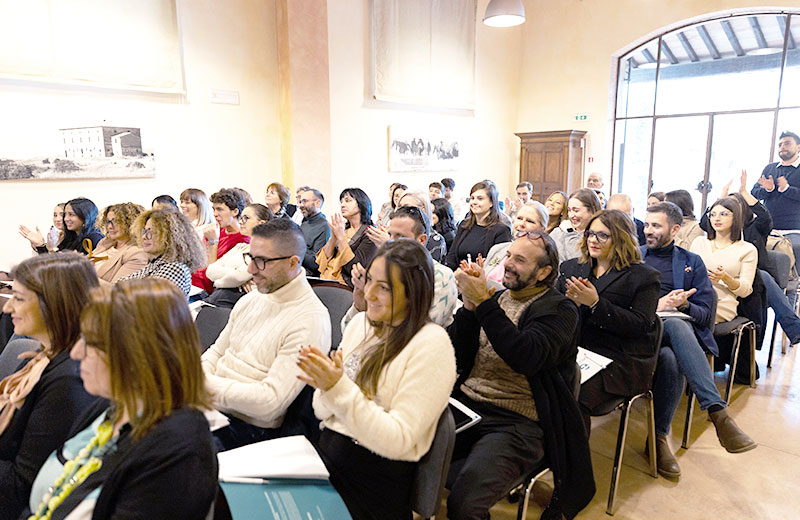 Pubblico che applaude e sorride durante un evento al chiuso in una luminosa sala conferenze.