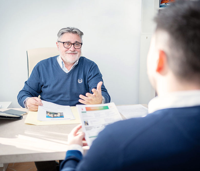 Due uomini discutono documenti in un ambiente d'ufficio luminoso.