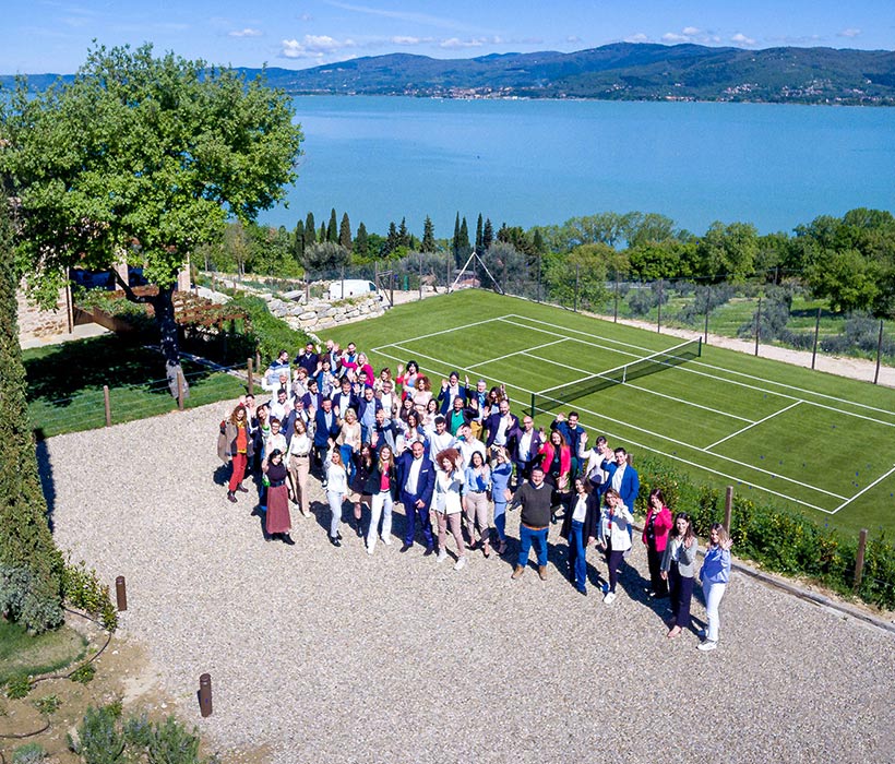 Vista aerea di un gruppo vicino a un campo da tennis con lago e colline sullo sfondo.