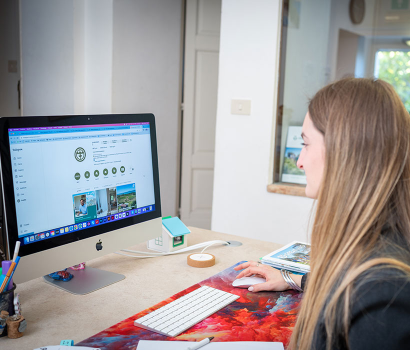 Donna lavora alla scrivania guardando una pagina social in un moderno ufficio domestico.