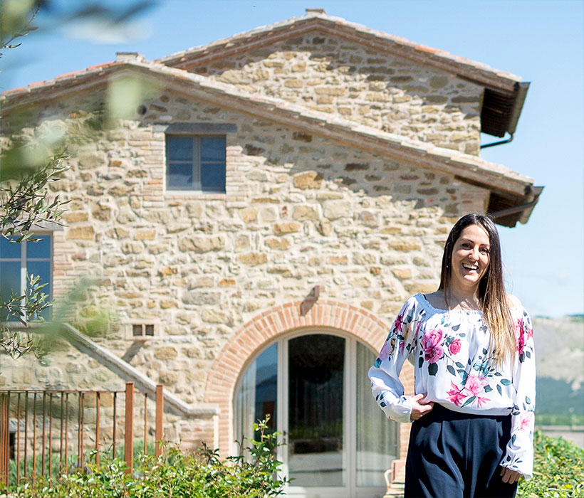 Каменный дом с арочным входом и улыбающейся женщиной в саду.