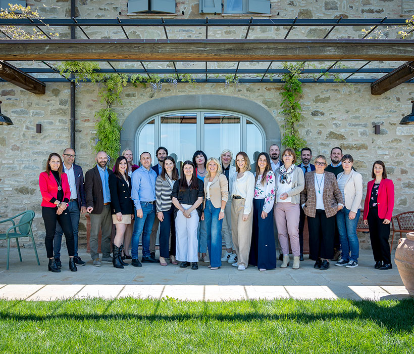 Группа людей позирует перед каменным зданием с зеленью.