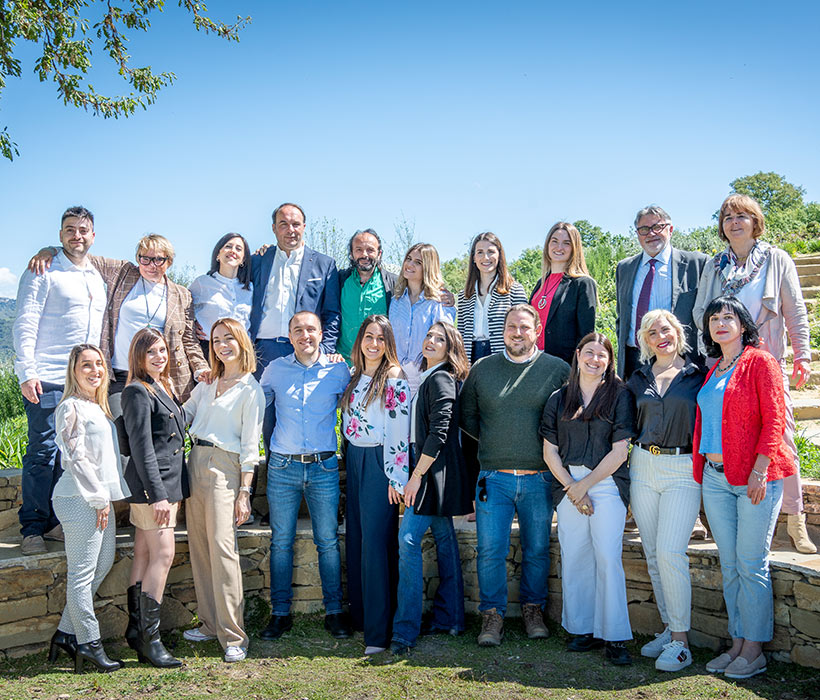 Gruppo di persone posa all'aperto in una giornata di sole con vegetazione sullo sfondo.