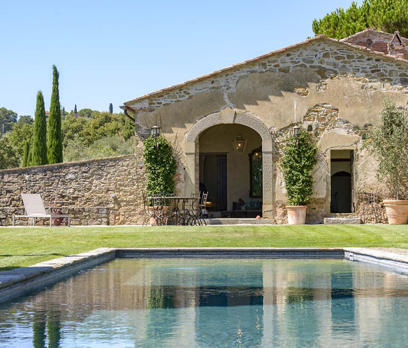 Casa in pietra rustica con ingresso ad arco, giardino e piscina in contesto panoramico.