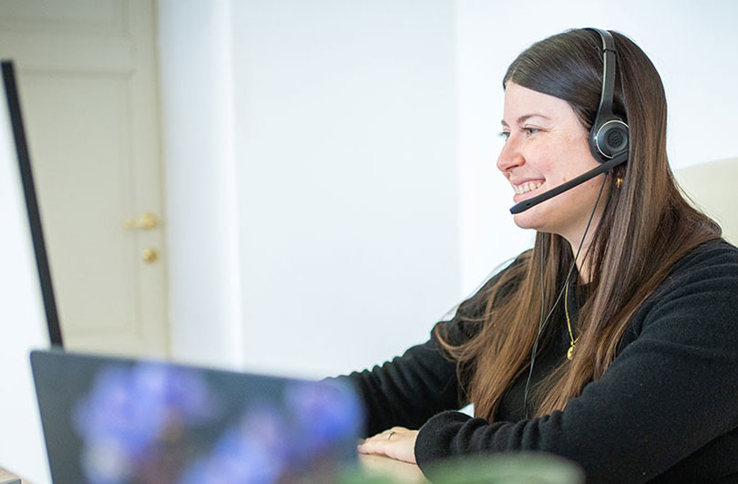 Donna sorridente alla scrivania con cuffie, ambiente d'ufficio di assistenza clienti.