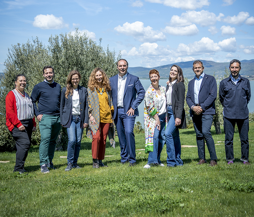 Группа людей стоит на зеленой лужайке на фоне деревьев и гор.