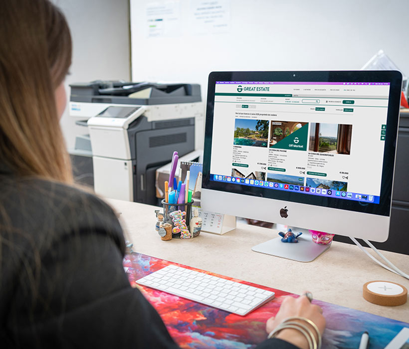 Persona che naviga gli annunci immobiliari di Great Estate su un computer desktop in ufficio.